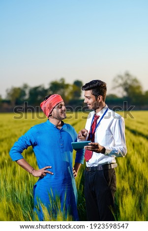 Young indian agronomist with farmer at green wheat field