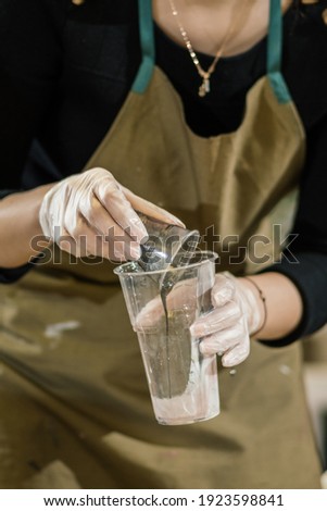 a girl in an apron and transparent gloves pours hot liquid from a small transparent glass into a large transparent glass