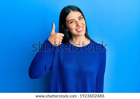 Young hispanic woman wearing casual clothes smiling happy and positive, thumb up doing excellent and approval sign 