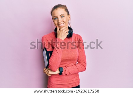 Beautiful caucasian woman wearing sportswear and arm band looking confident at the camera smiling with crossed arms and hand raised on chin. thinking positive. 