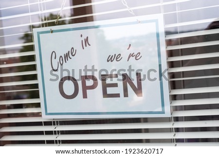 Come in we're open sign hanging behind a store window