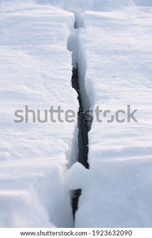 Vertical outdoor dramatic photo of a crack in the ice on a frozen lake at winter daytime