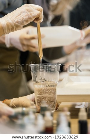 a wooden stick is lowered into a glass with transparent resin and the resin flows down in a thin stream back into the glass