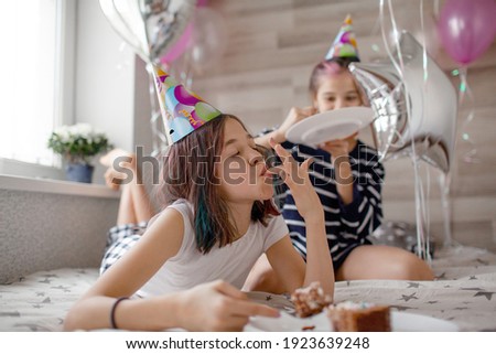 Two preteen sisters twins celebrate birthday day at the morning, active kids dressed in pajamas have fun in the bed with balloons. Children eat cake in the bed