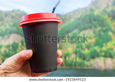Woman holding a black cup with coffee on the background of a beautiful landscape.