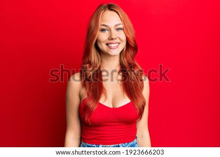 Young beautiful redhead woman wearing casual clothes over red background with a happy and cool smile on face. lucky person. 