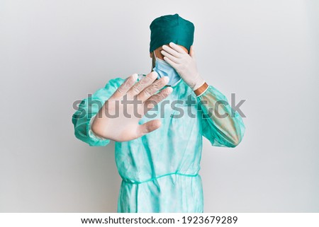 Young handsome man wearing surgeon uniform and medical mask covering eyes with hands and doing stop gesture with sad and fear expression. embarrassed and negative concept. 