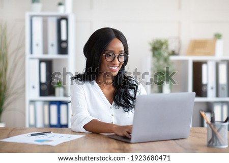 Beautuful black businesswoman working with laptop computer at desk in office. African American female entrepreneur typing document, checking email, participating in online meeting at workplace Royalty-Free Stock Photo #1923680471