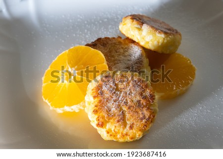 Sweet cottage cheese pancake sprinkled with powdered sugar with orange close-up on a white plate. Concept of a delicious, healthy breakfast