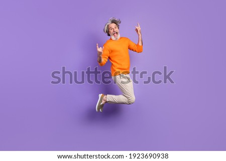 Full size photo of young crazy funky funny smiling old man jumping showing rock'n'roll sign isolated on violet color background