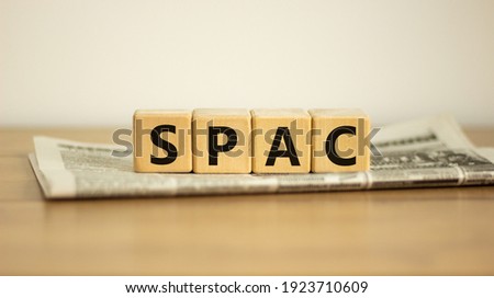 SPAC, special purpose acquisition company symbol. Wooden cubes with word 'SPAC' on beautiful white background, copy space. Newspaper. Business and SPAC, special purpose acquisition company concept.