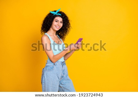 Photo of adorable shiny wavy lady dressed turquoise tank-top holding modern gadget empty space isolated yellow color background