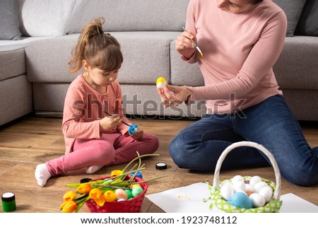 A mother and her daughter painting Easter eggs at home.