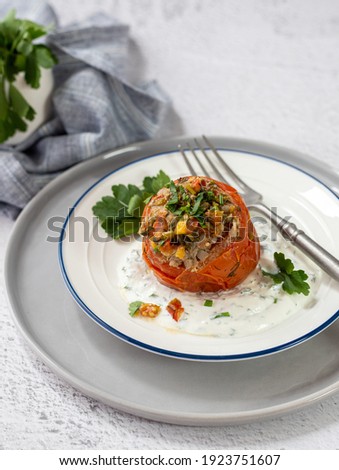 Tomatoes stuffed with ground meat and buckwheat cereal, served in white ceramic plate with sour cream sauce and micro greens