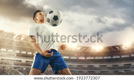 Junior football or soccer player at stadium in flashlight. Young male sportive model training. Moment of attacking, catching. Concept of sport, competition, winning, action, motion, overcoming.