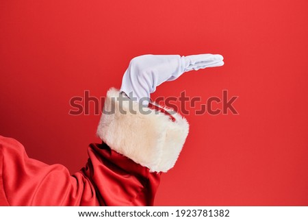 Hand of a man wearing santa claus costume and gloves over red background with flat palm presenting product, offer and giving gesture, blank copy space 