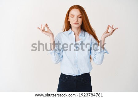 Image of young redhead woman keeping calm with meditation, close eyes and spread hands in mudra om sign, practice yoga against white background.