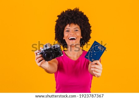 mixed afro woman with a photo camera photography and brazilian passport in yellow background

