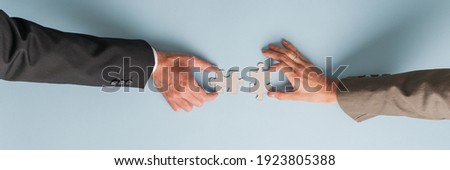 Wide view image of male and female hand joining two blank matching puzzle pieces. Over light blue background. Royalty-Free Stock Photo #1923805388