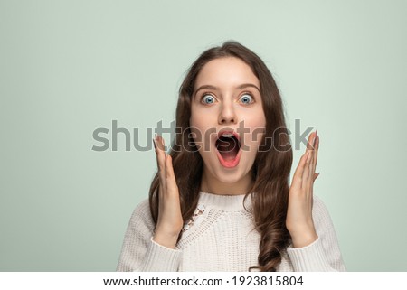 Close up portrait of beautiful darkhaired woman spreading hands, standing isolated over background, astonished female with widely opened mouth wearing ssweater. People emotions concept. Royalty-Free Stock Photo #1923815804