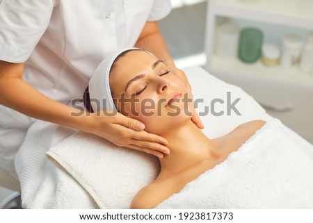 Hands of cosmetologist making manual relaxing rejuvenating facial massage for young woman in beauty salon. Rejuvenating facial massage in cosmetology Royalty-Free Stock Photo #1923817373