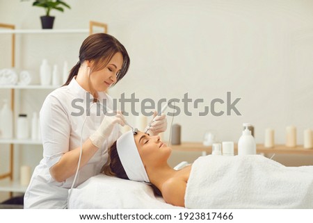 Beautician makes a young beautiful girl a vacuum facial treatment for rejuvenation. Girl is undergoing a course of spa treatments in the office of a beautician. Royalty-Free Stock Photo #1923817466