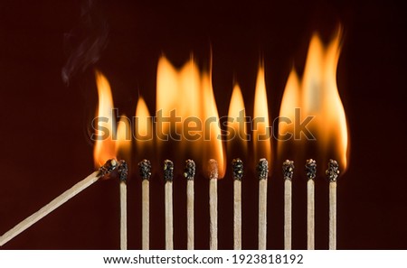 Lit match next to a row of lighting matches. Red phosphorus matches on dark red background. Concept of ignition or initiation Royalty-Free Stock Photo #1923818192