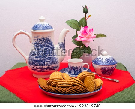 breakfast with chocolate cookies, cup of coffee, coffee or tea pot and vase with pink flowers.
