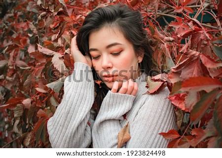 brunette with a Japanese appearance in a light sweater on a background of red autumn leaves
