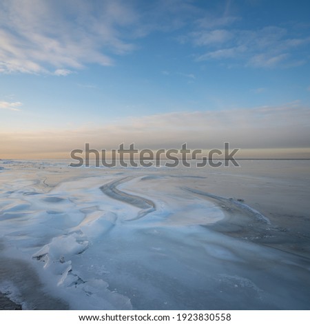 Square landscape with a track on the ice in the sea bay against the background of the orange-blue sunset sky in winter