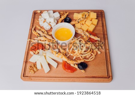 Wine appetizer set. Cherry-tomatoes, parmesan cheese, meat variety, bread slices, dried tomatoes, olives and basil on round ceramic plate over white wood backdrop, top view.