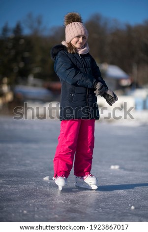 pretty cheerful little girl in thermal suits skating outdoors