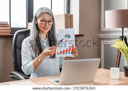 Beautiful mature caucasian woman showing charts during video call at the office desk