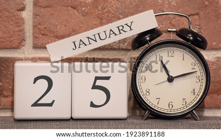 Important date, January 25, winter season. Calendar made of wood on a background of a brick wall. Retro alarm clock as a time management concept.