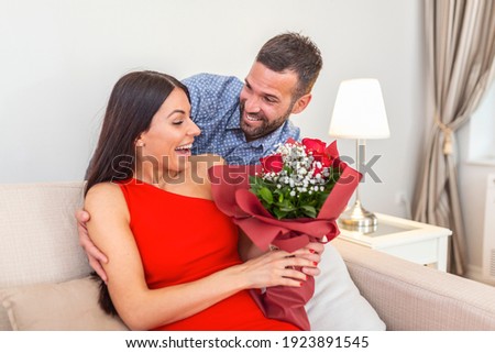 Affectionate young man giving his beautiful young wife a bouquet of red roses on Valentines day to surprise his girlfriend, romantic happy couples sharing gift together on Valentines day