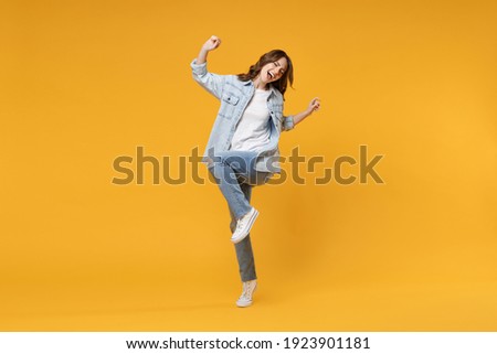 Full length of young overjoyed excited fun student happy woman 20s in denim shirt white t-shirt do winner gesture clench fist celebrating dancing isolated on yellow color background studio portrait.