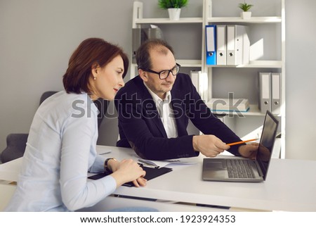 Real estate agent meeting with client at his office. Realtor helping future buyer make right choice. Serious single woman considering house variants and apartment options on laptop computer screen