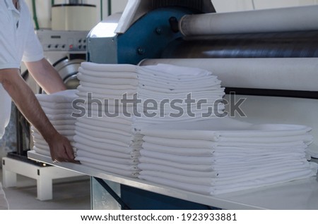 Unrecognizable man stacking freshly ironed sheets or fabrics in an industrial laundry. Cleaning and ironing service for hotels, clinics and companies.