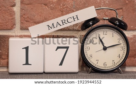 Important date, March 17, spring season. Calendar made of wood on a background of a brick wall. Retro alarm clock as a time management concept.