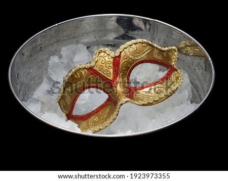 Traditional golden carnival Venetian mask with red ornaments in a bucket with crushed ice cubes. Brazilian Mardi Gras Festival. The concept of a hot parade, masquerade.