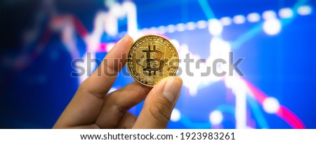 A hand of people is holding bitcoin (btc, xtc) coin in metallic golden color with declined stock graph as blurred background. Business and finance investment failure concept photo.