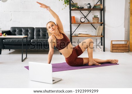 Sporty young woman with perfect athletic body wearing sportswear watching online stream on laptop and exercising during workout training. Concept of healthy lifestyle and physical activity at home.