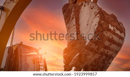 Backhoe digging soil at construction site. Dirt bucket of backhoe digging soil with yellow sunset sky. Crawler excavator digging on soil. Excavating machine. Earth moving machine. Excavation vehicle. Royalty-Free Stock Photo #1923999857