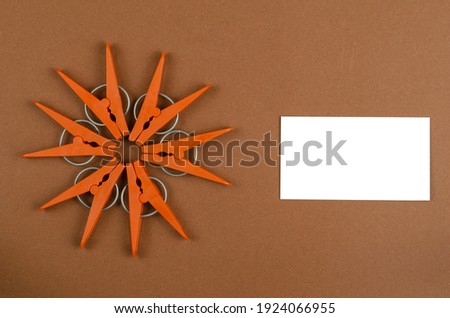 Geometric star shape made from brown plastic clothespins and white blank business card on brown background. Laundry service, housekeeping. Top view, flat lay