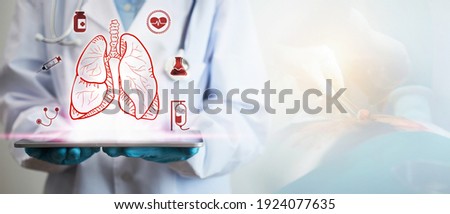 Concept of lung disease treatment. A doctor's hand is holding a tablet showing a lung icon, along with the background is a picture of the thoracic surgery blurred with light.