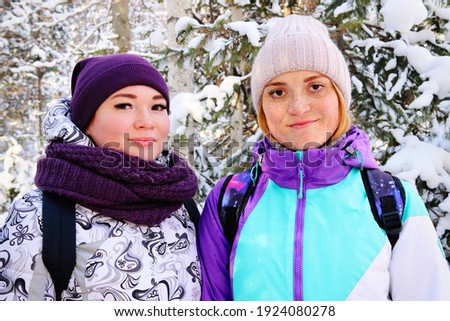 A vivid portrait of two beautiful girls tourists on a winter hike in the mountains of the Urals. Girls in the winter spruce forest covered with snow. Aygir, Republic of Bashkortostan, Russia.