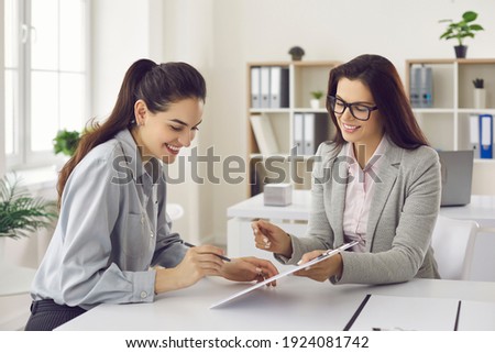 Happy female client signs a lease or purchase agreement given to her by a bank manager or real estate agent. Before signing the woman reads the terms of the mortgage, lease or purchase agreement. Royalty-Free Stock Photo #1924081742