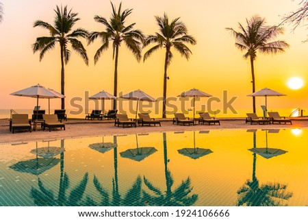 Umbrella and chair around outdoor swimming pool with sea beach ocean at sunset or sunrise time