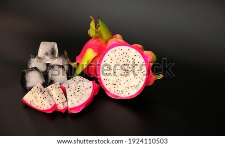 Ripe cut fruit of exotic fruit Pitaya or Dragon Heart with ice cubes on a black background. Close-up.