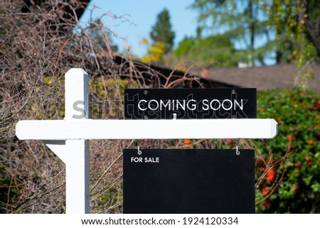 COMING SOON sign near a house for sale in a residential neighborhood. Green trees background.